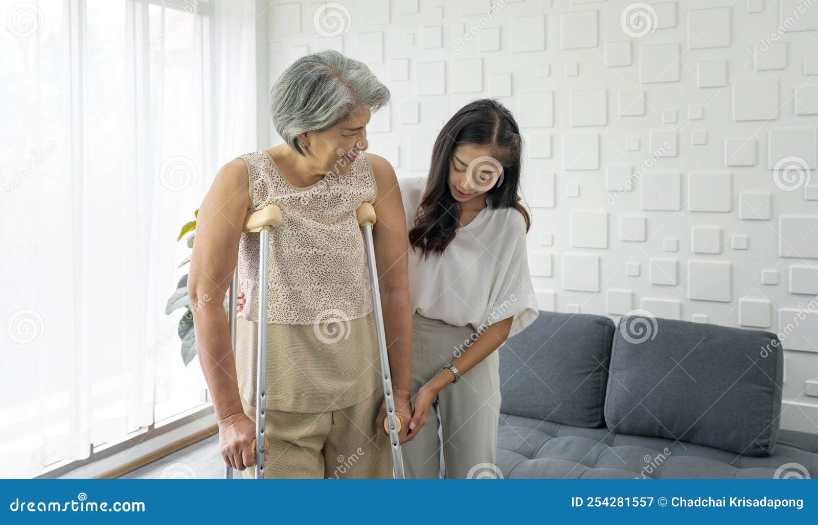 young asian woman help her grandma walk by using axilla crutches. senior gray hair woman exercise and practice walking at home