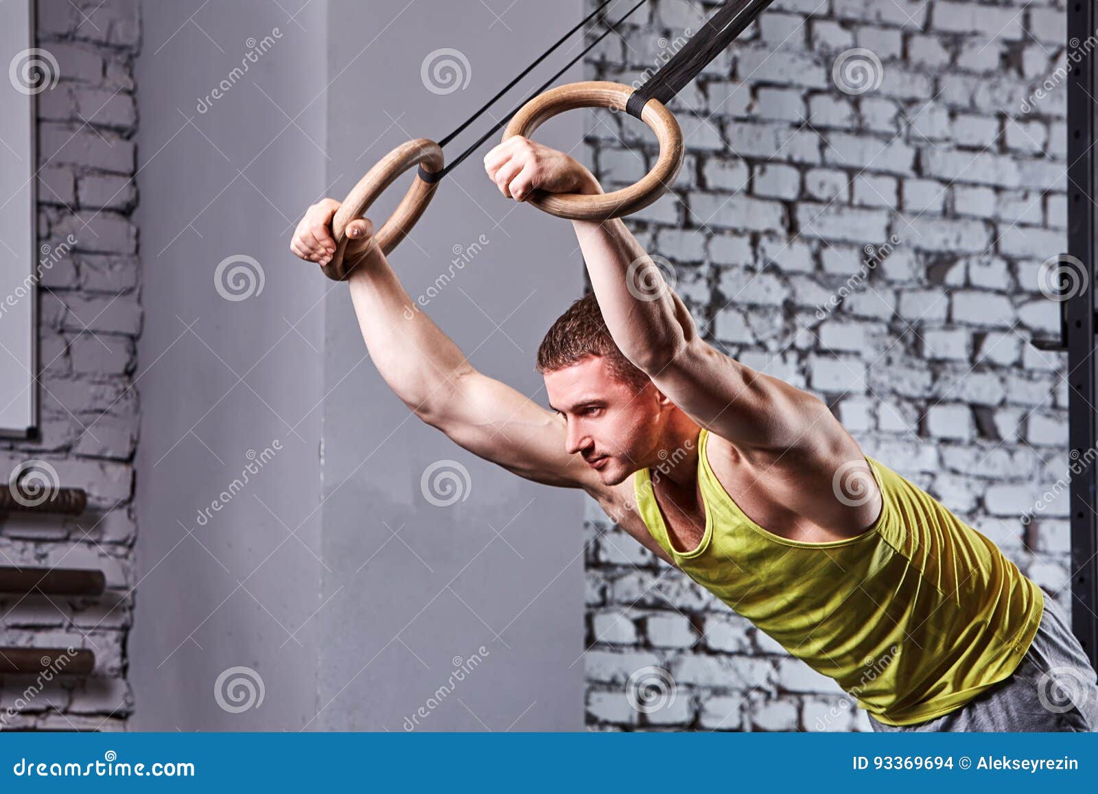 young athlete man in the sportwear pulling up on gymnastic rings against brick wall in the cross fit gym.