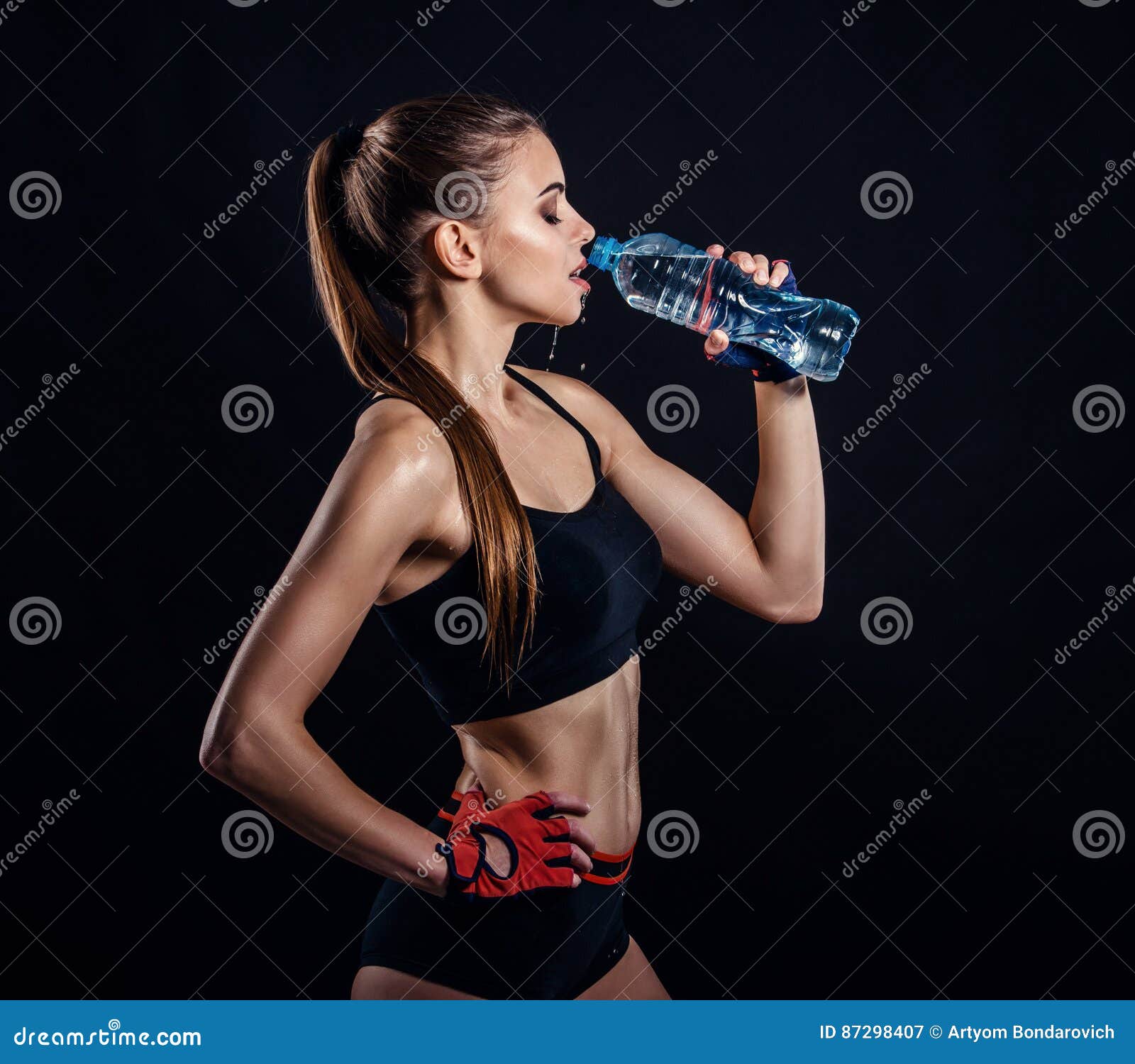 Young athletic woman in sportswear posing in studio against black  background. Ideal female sports figure. Fitness girl with perfect sculpted  muscular and tight body. Stock Photo