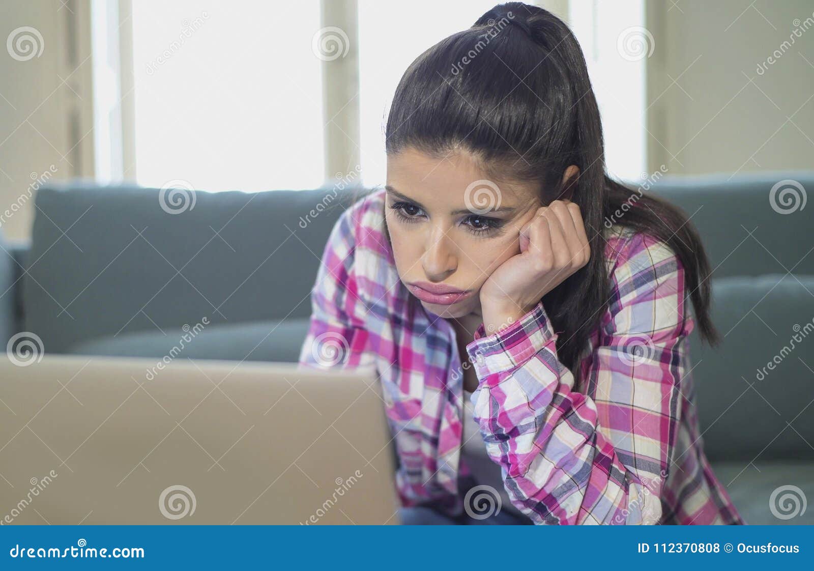 young attractive and bored latin woman on her 30s working at home living room sitting on couch with laptop computer in stress look
