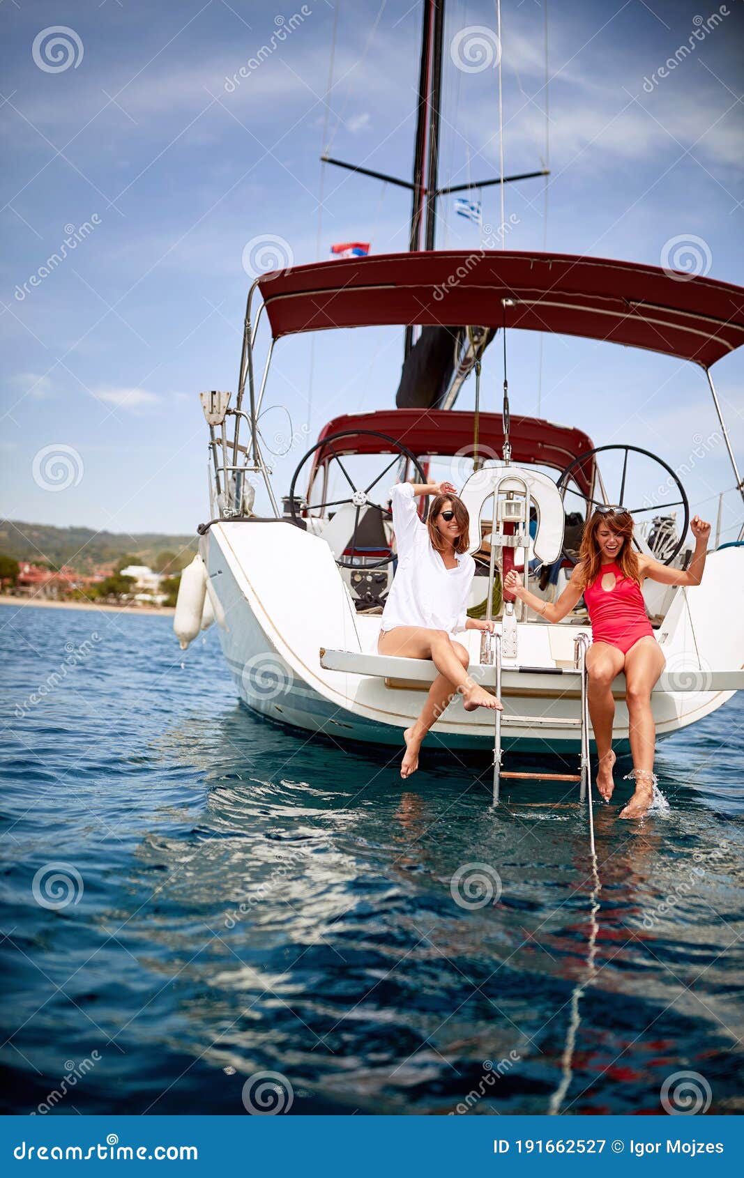 young attractive girls on stern of a yact cooling legs in the sea