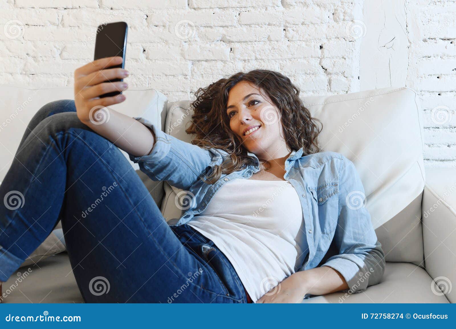Young Attractive Hispanic Woman Lying On Home Couch Taking Selfie Photo 
