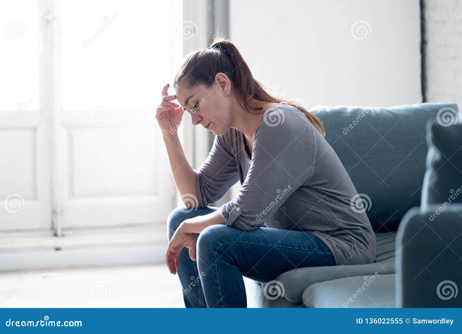 young woman suffering from depression feeling sad and lonely on sofa at home