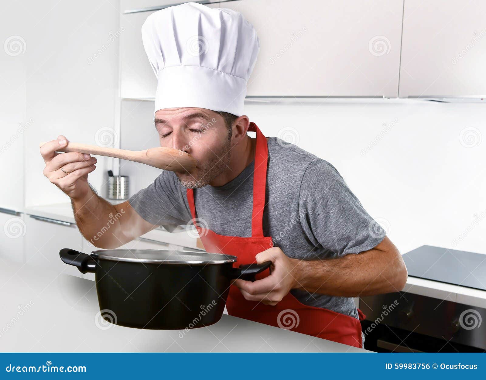 Young Attractive Man In Chef Hat And Red Cook Apron Testing Flavor