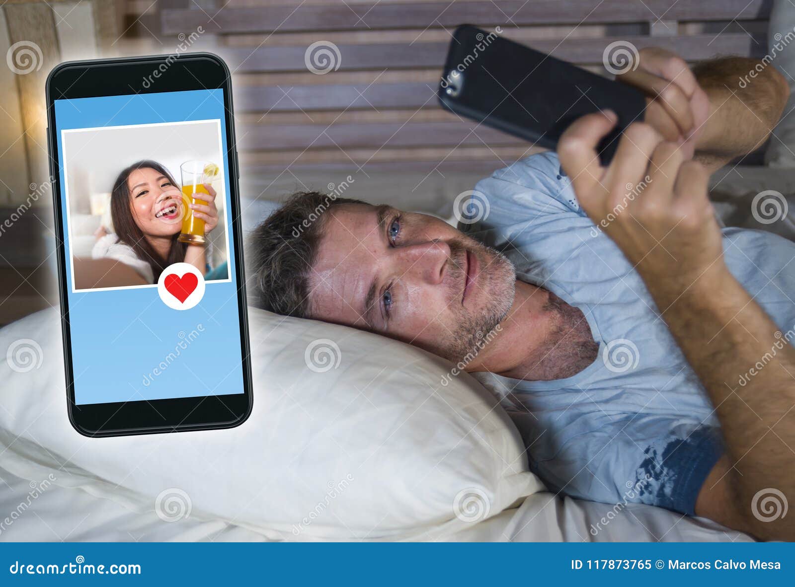 Young Attractive Man Lying in Bed on Line Searching for Sex or Love Finding a Beautiful Girl Profile Sending Like Using Mobile Pho Stock Image photo