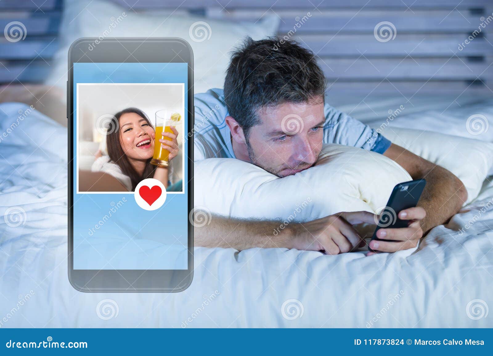 Young Attractive Man Lying in Bed on Line Searching for Sex or Love Finding a Beautiful Girl Profile Sending Like Using Mobile Pho Stock Photo photo