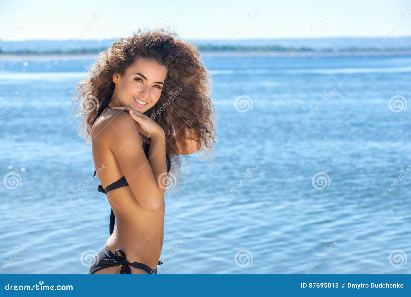 young, attractive, smiling slender girl with curly hair in a black bathing suit on the beach