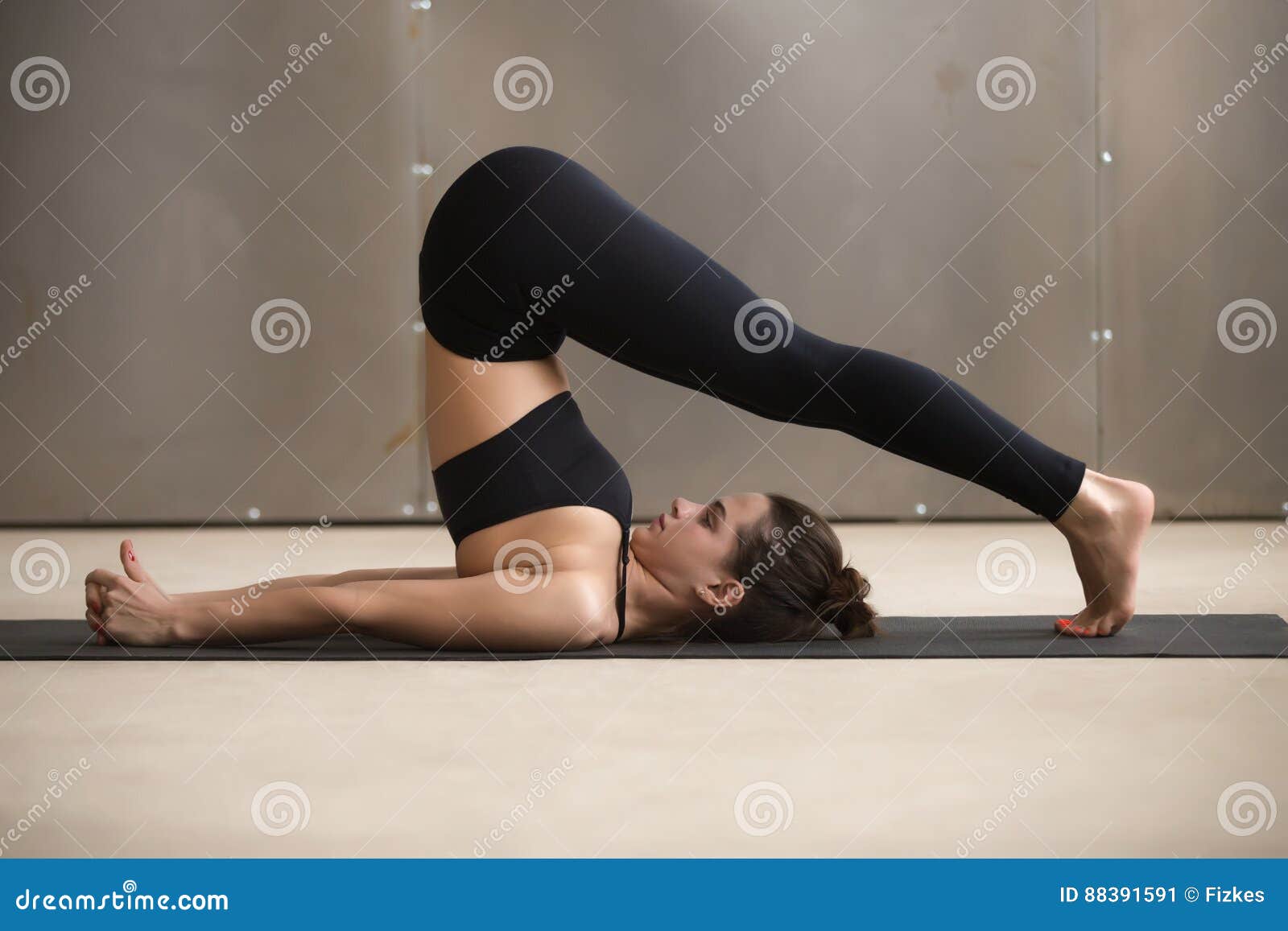 young attractive woman stretching in halasana pose, grey studio