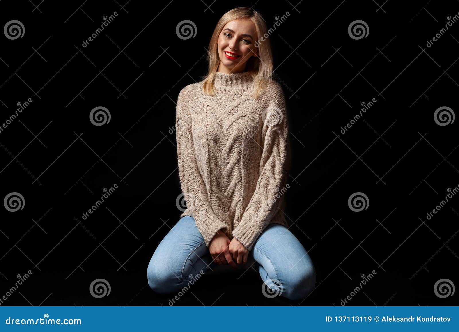 Young Beautiful Blonde Woman In Knitted Beige Sweater Blue Jeans Kneeling On The Floor With