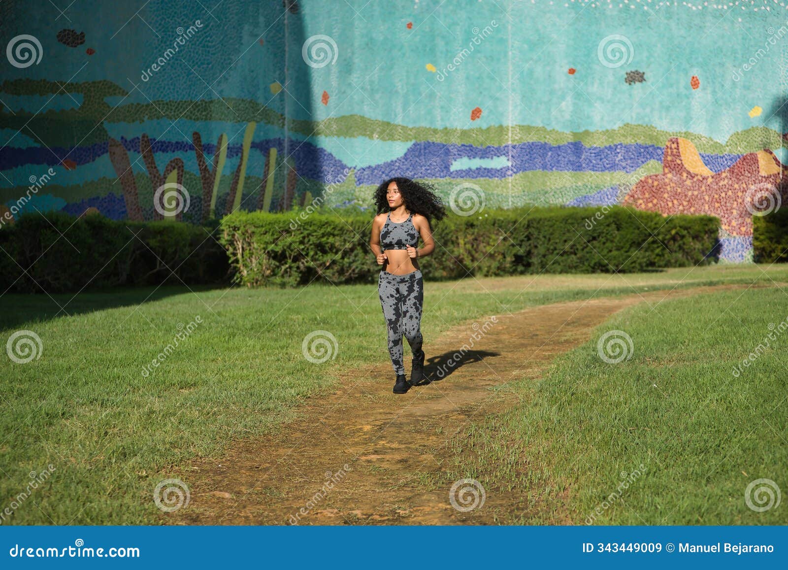 young, beautiful, brunette, latina woman with curly hair and sport clothes, running happily and contentedly in an open-air park.