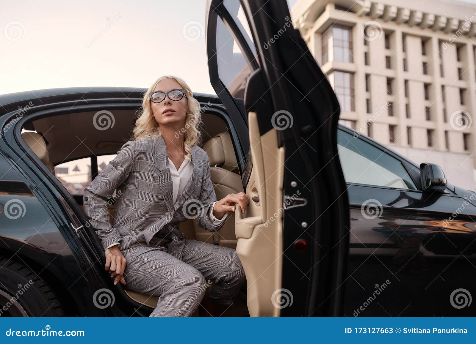 young beautiful business woman in stylish suit getting out of a black car