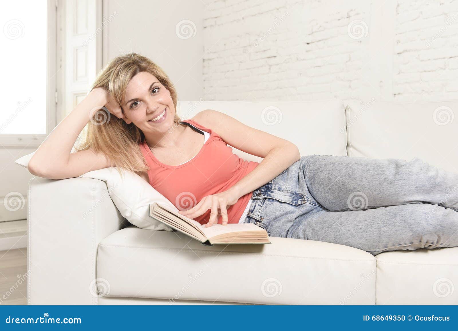 young beautiful caucasian woman reading book studying lying comfortable on home sofa looking happy