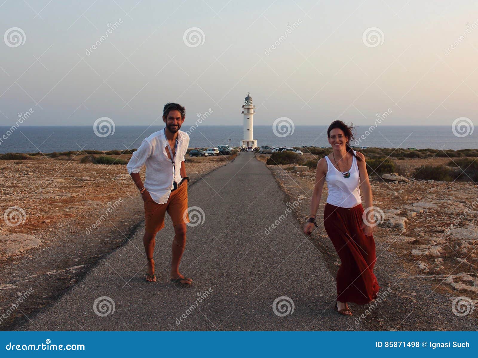 young beautiful couple`s portrait with cap de barberia`s lighthouse on soft background, formentera, balearic islands, spain
