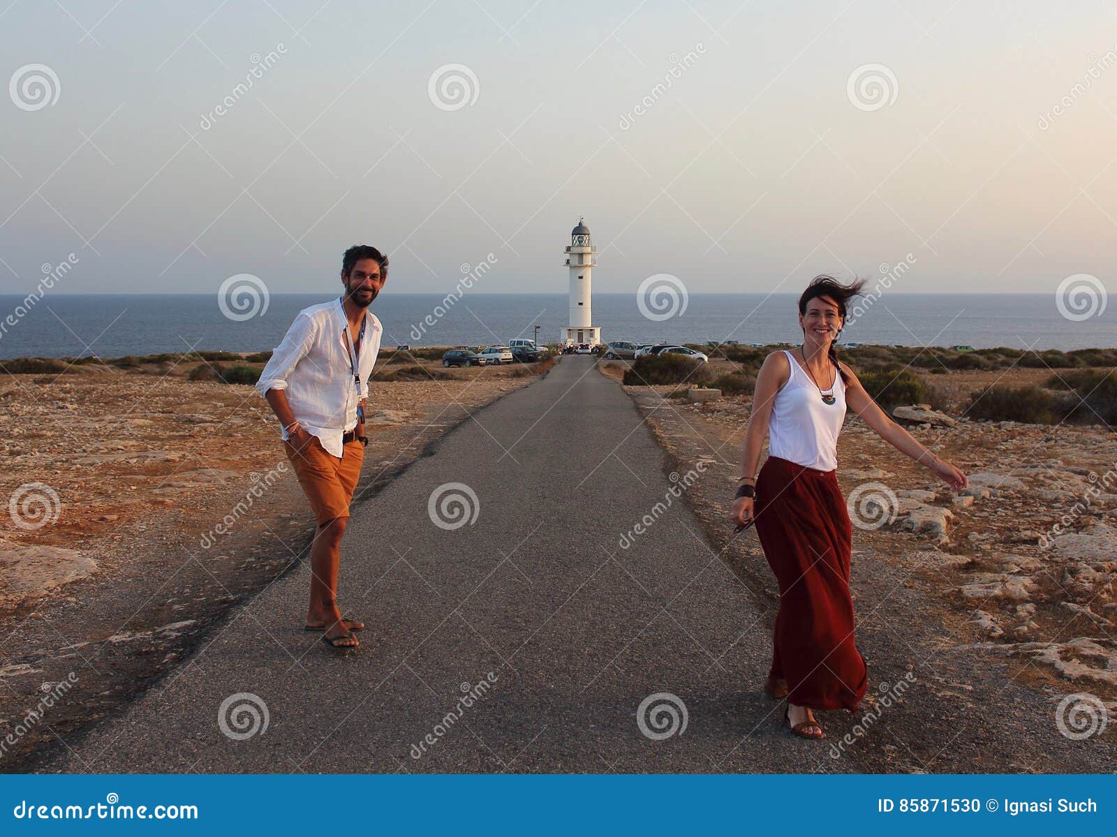young beautiful couple`s portrait with cap de barberia`s lighthouse on soft background, formentera, balearic islands, spain