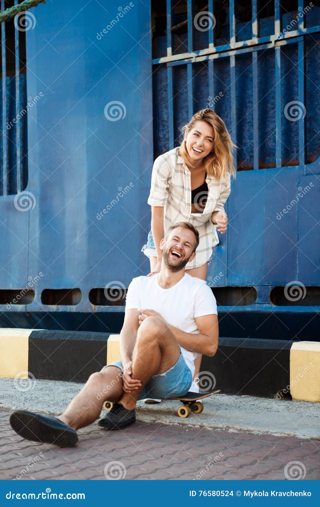 Young beautiful couple walking around city, smiling, sitting on skates. Outdoor background.