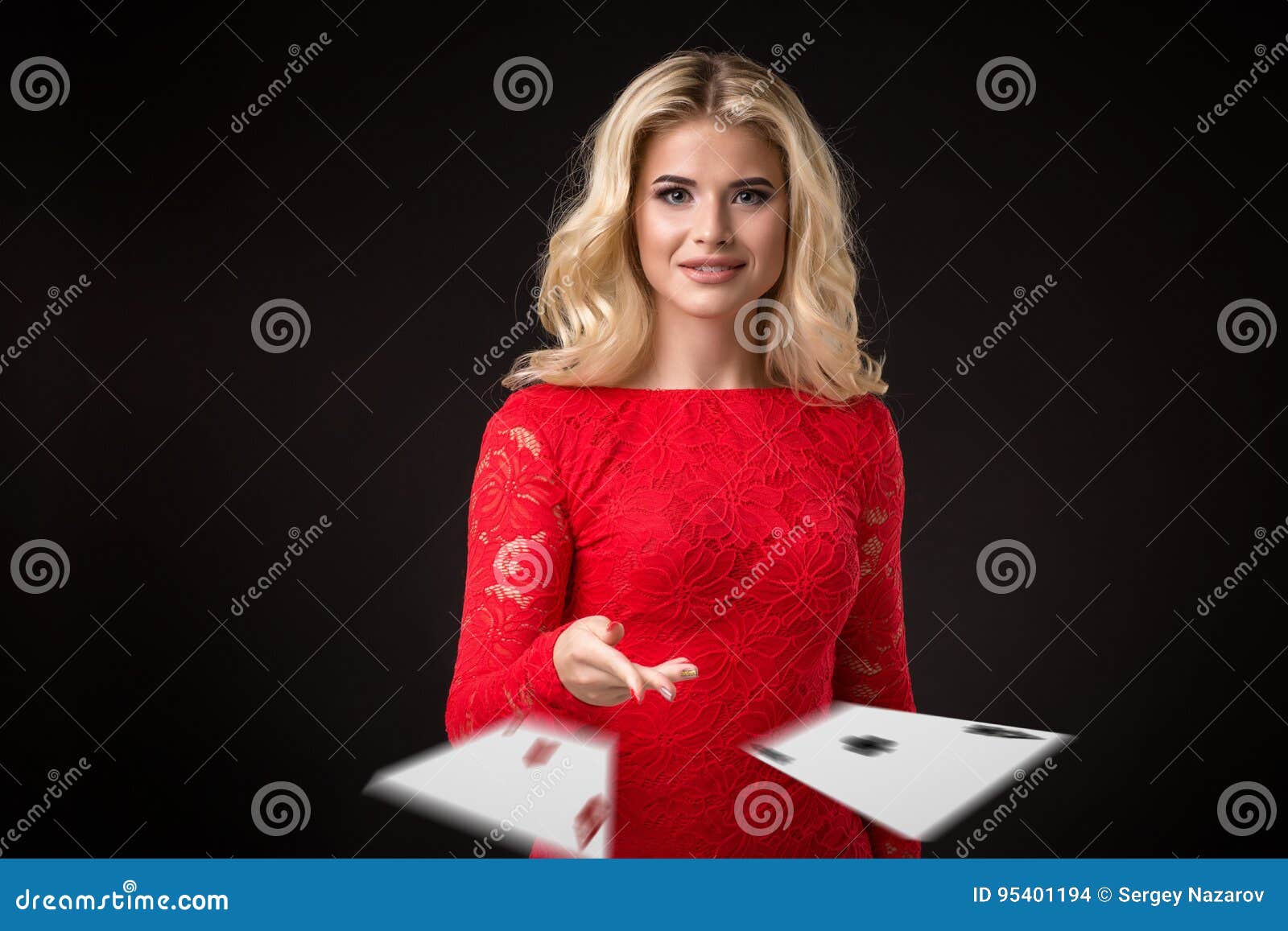 Young beautiful emotional woman throws cards on a black background in the studio. Poker. Young beautiful emotional woman throws two aces cards on a black background in the studio. Portrait of a beautiful blonde in a red dress. Poker