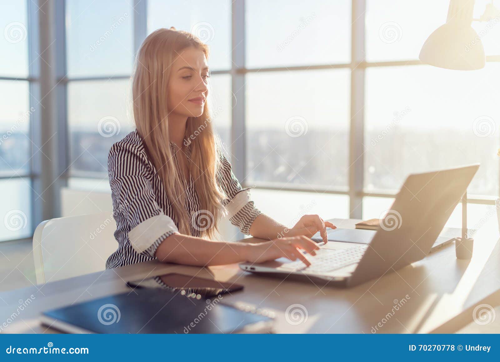 young beautiful female copywriter typing texts and blogs in spacious light office, her workplace, using pc keyboard
