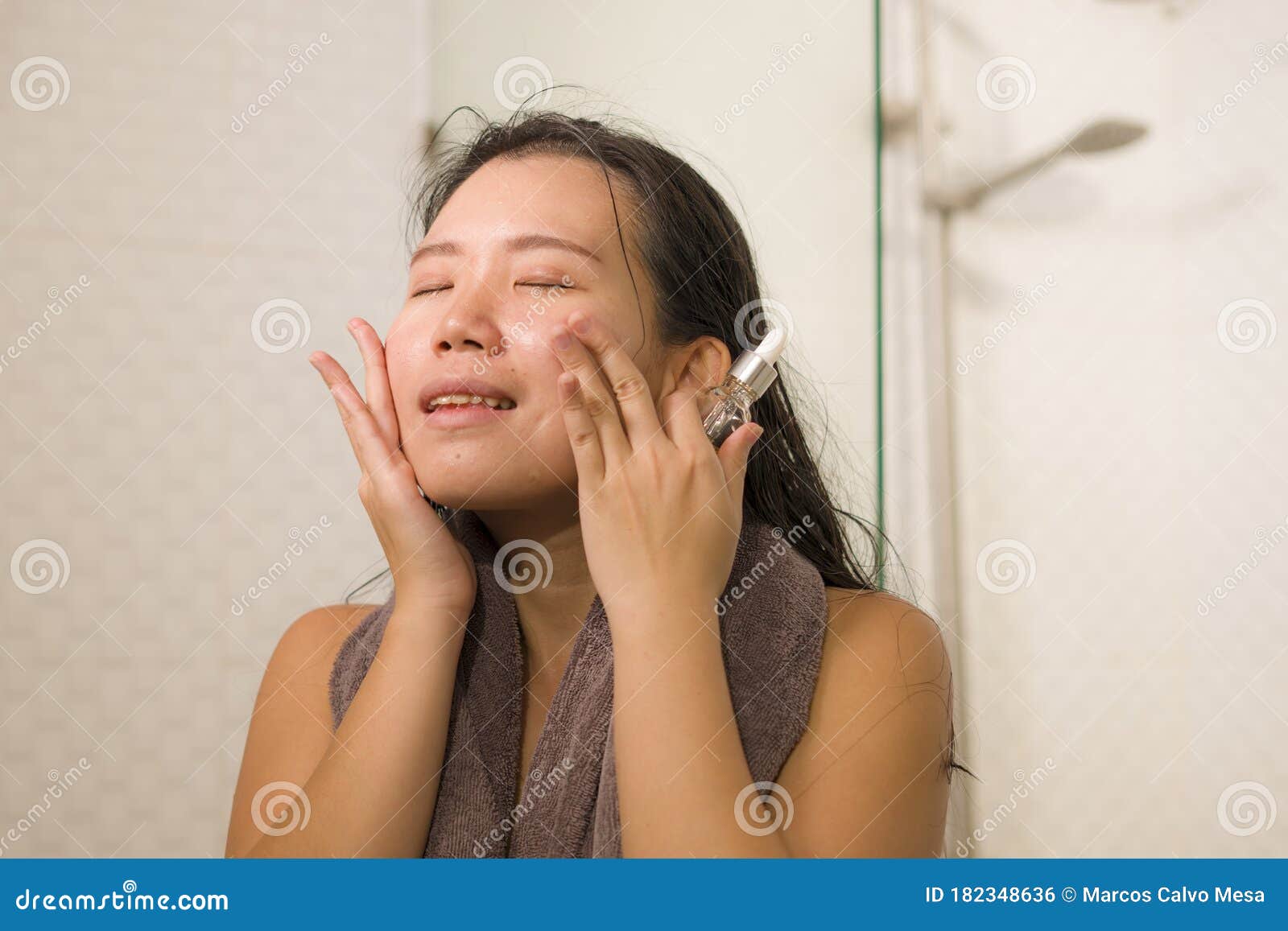 young beautiful and happy asian chinese woman applying serum facial skin care and face treatment in the bathroom enjoying morning