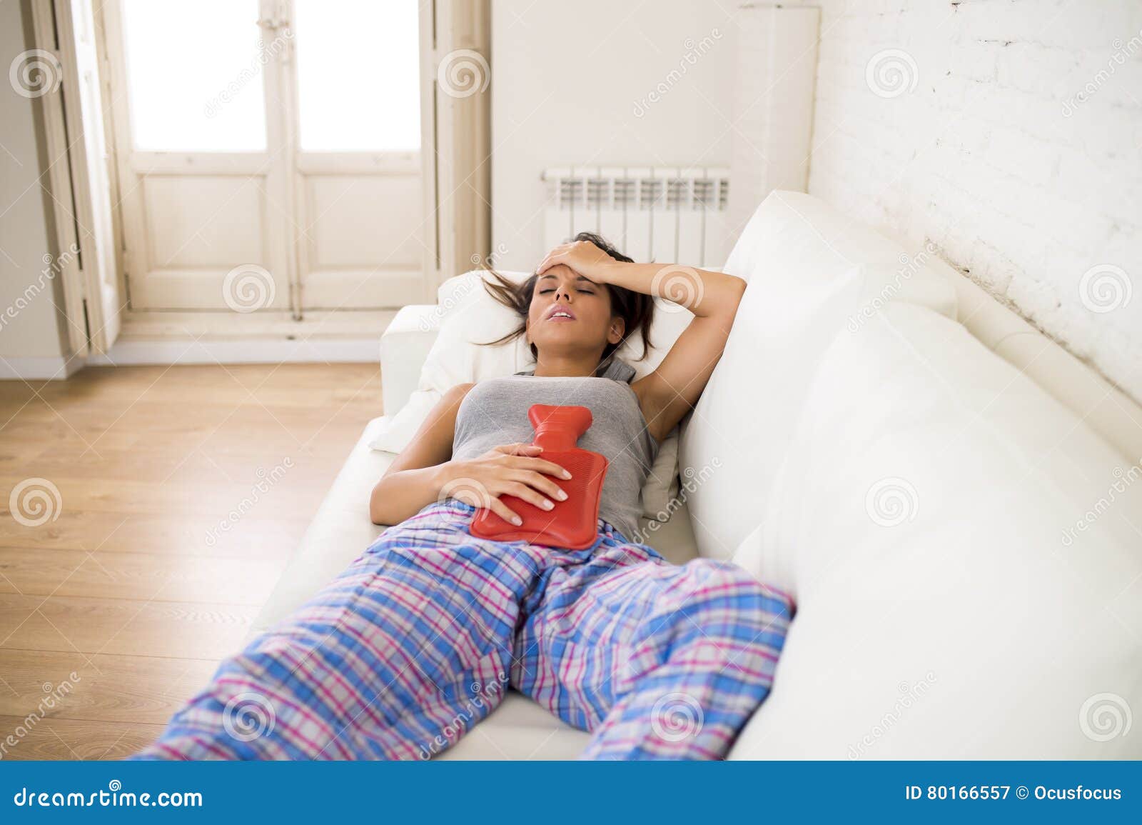 young beautiful hispanic woman holding hot water bottle against belly suffering menstrual period pain