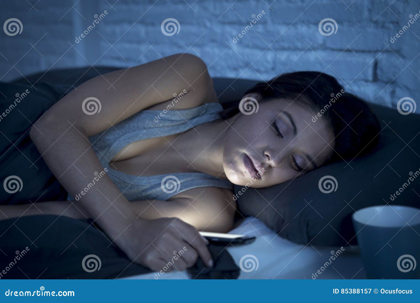 young beautiful latin woman on bed late at night texting using mobile phone tired falling sleep