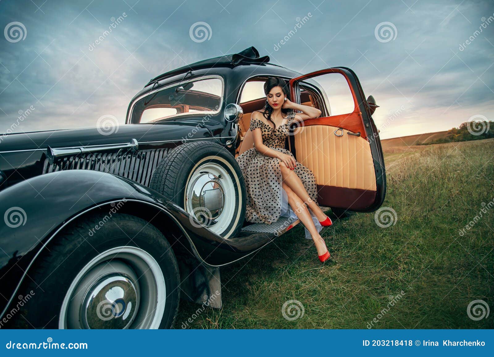 young beautiful sexy woman in pin-up style clothes sits posing in black retro car. polka dot white dress, vintage