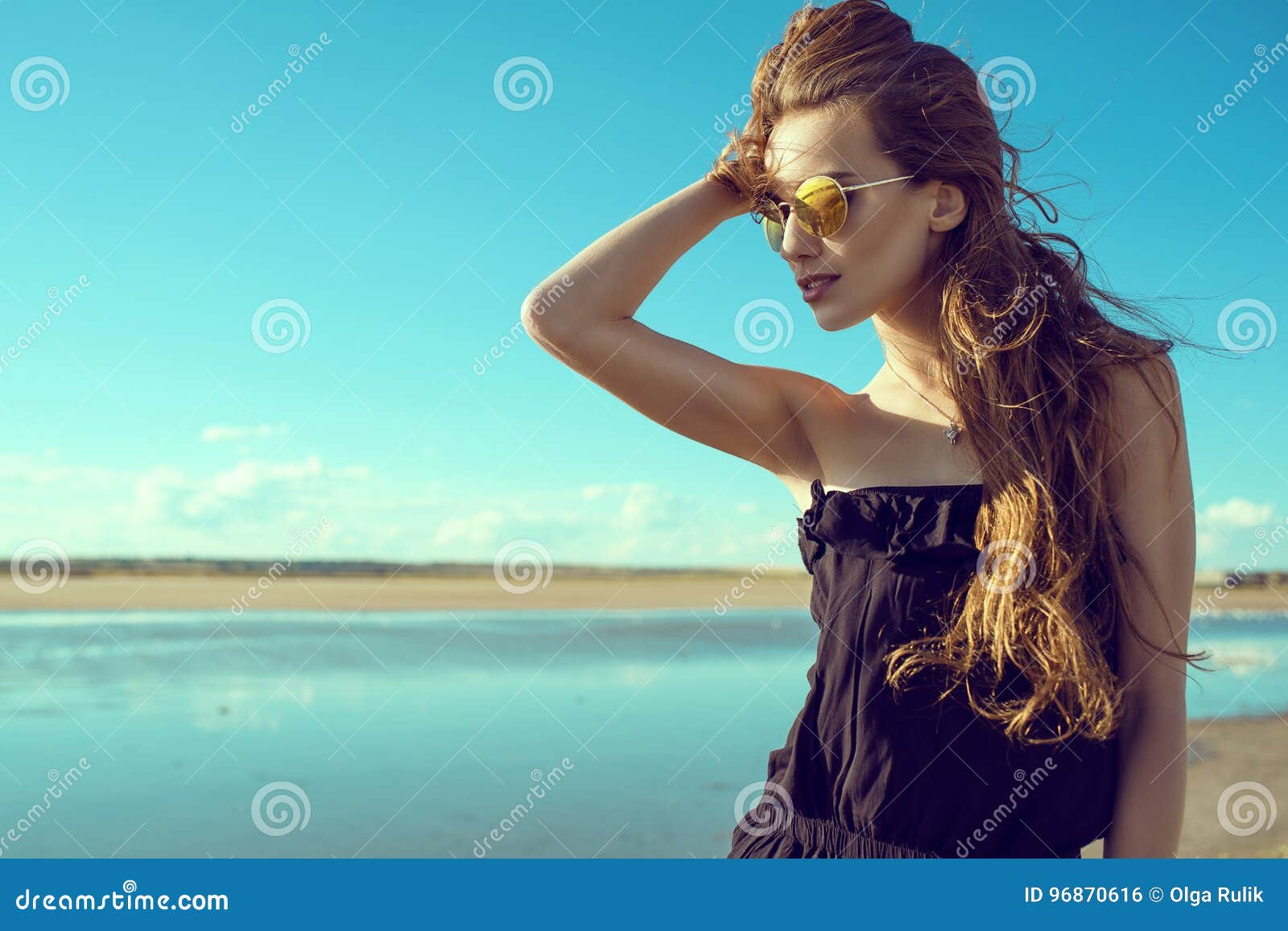 young beautiful stylish woman wearing black open shoulder romper and trendy round mirrored sunglasses standing at the pool