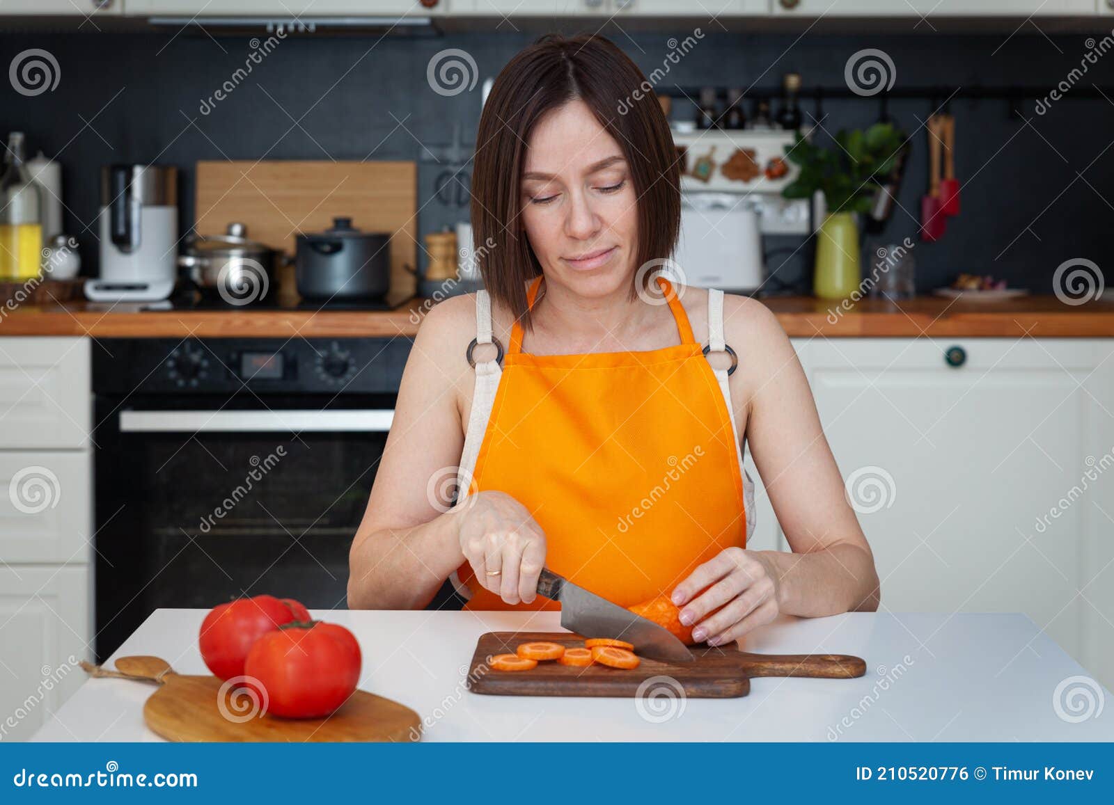 Young Beautiful Woman In Apron Sitting At Table Cooking At Home 