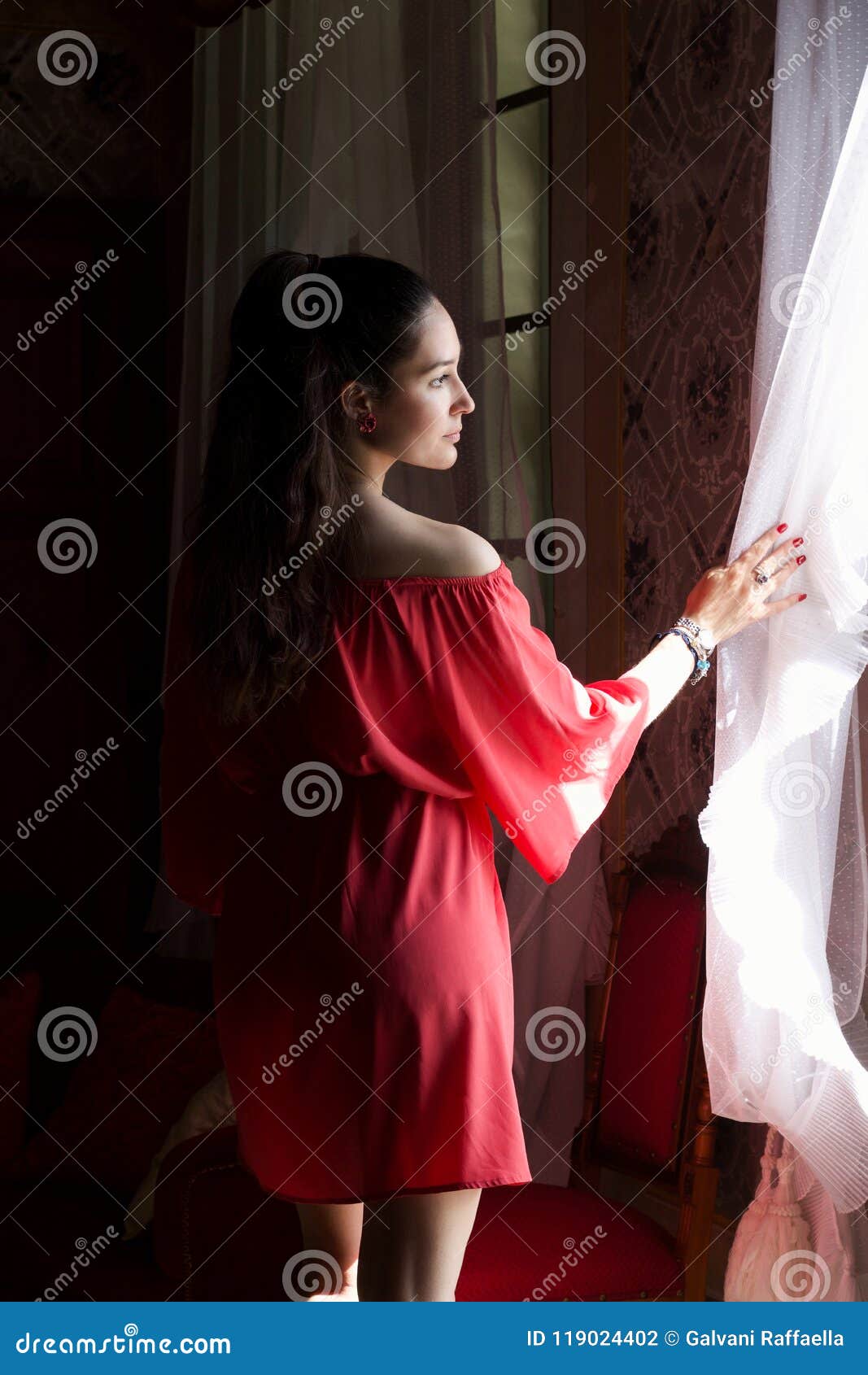 young beautiful woman in coral silk dress looking through a win