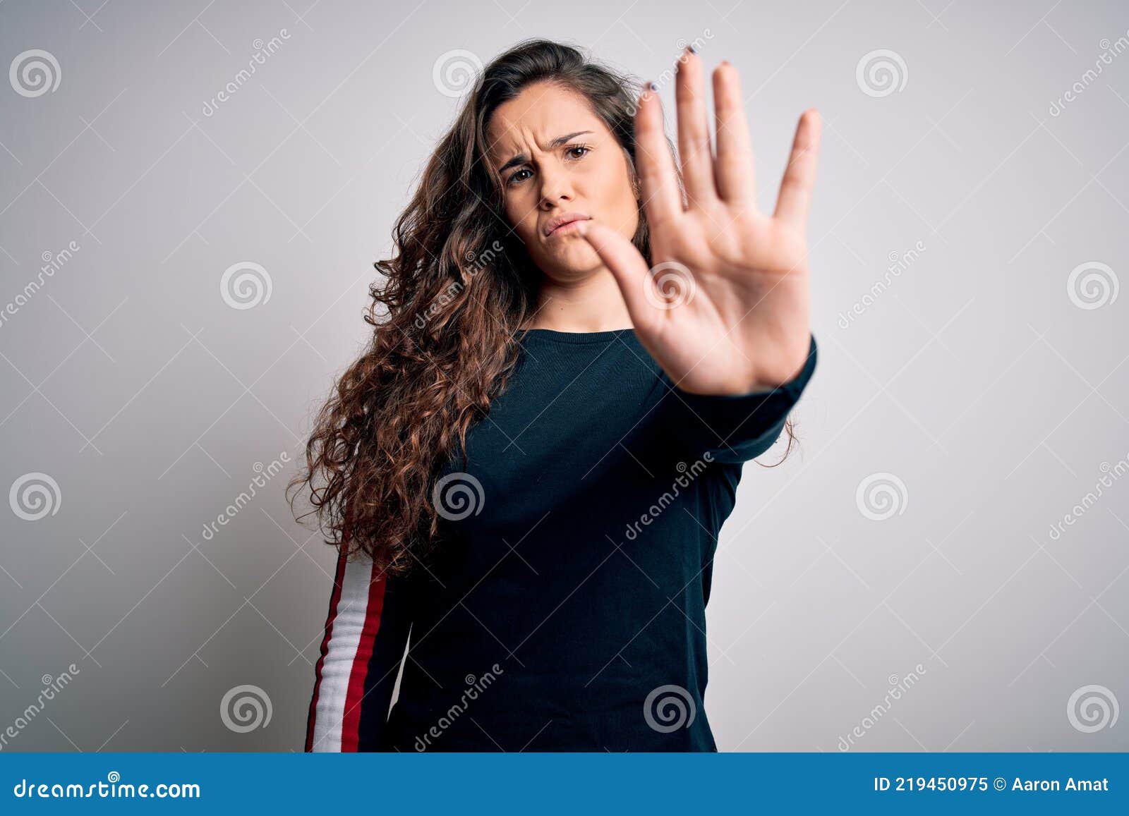 young beautiful woman with curly hair wearing casual sweater over  white background doing stop sing with palm of the hand