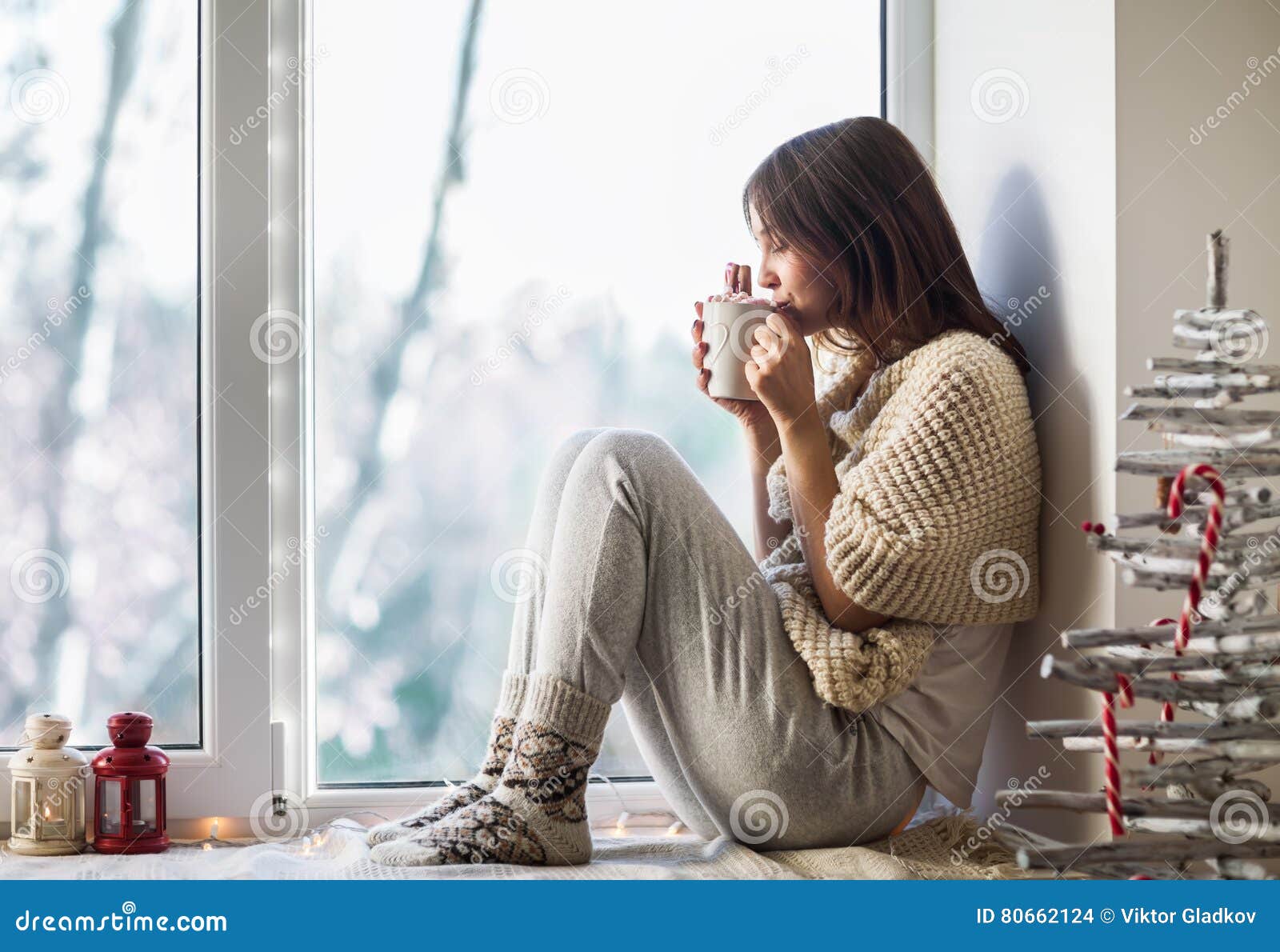 young beautiful woman drinking hot coffee sitting on window sill