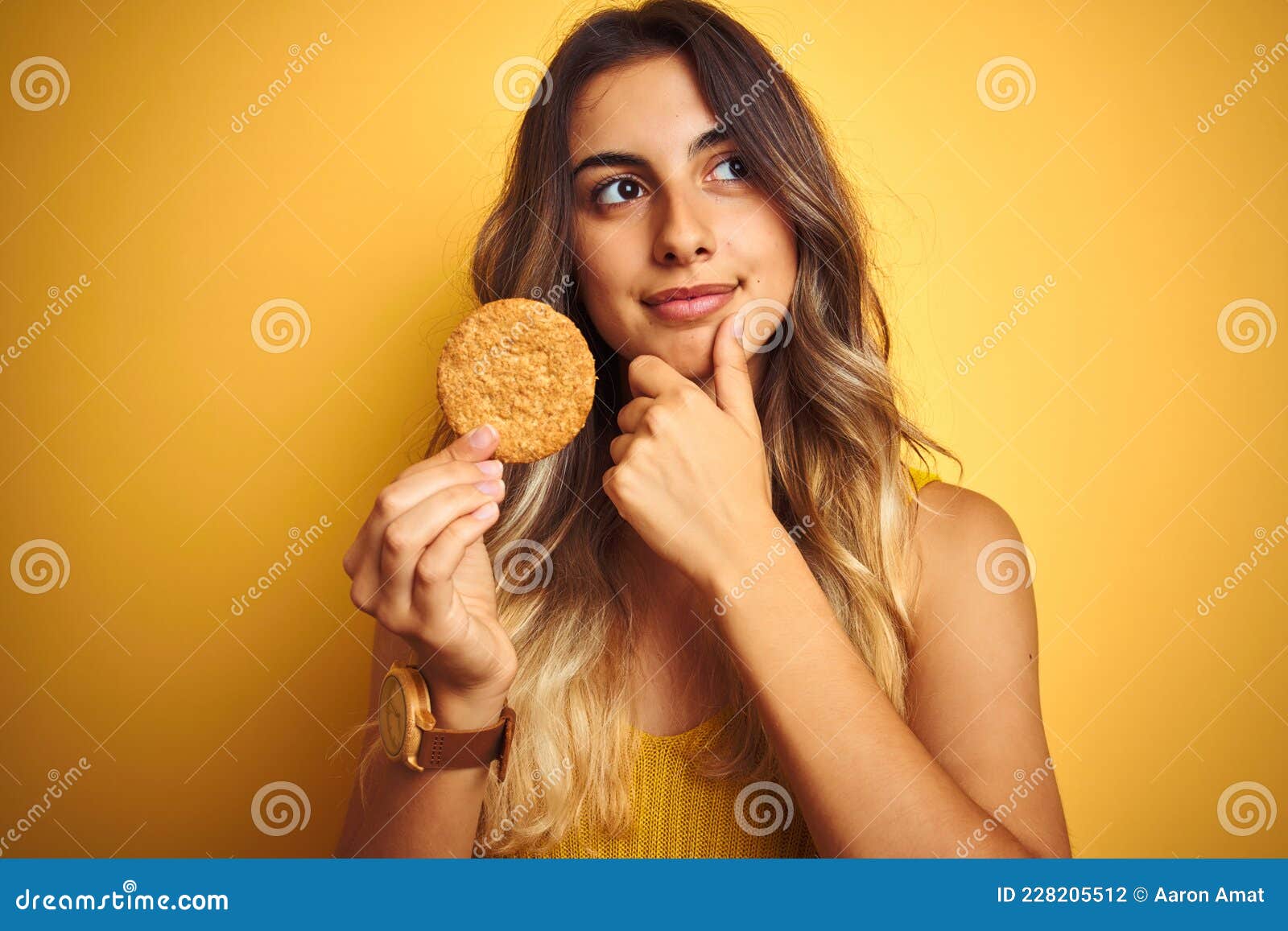 young beautiful woman eating biscuit over grey  background serious face thinking about question, very confused idea