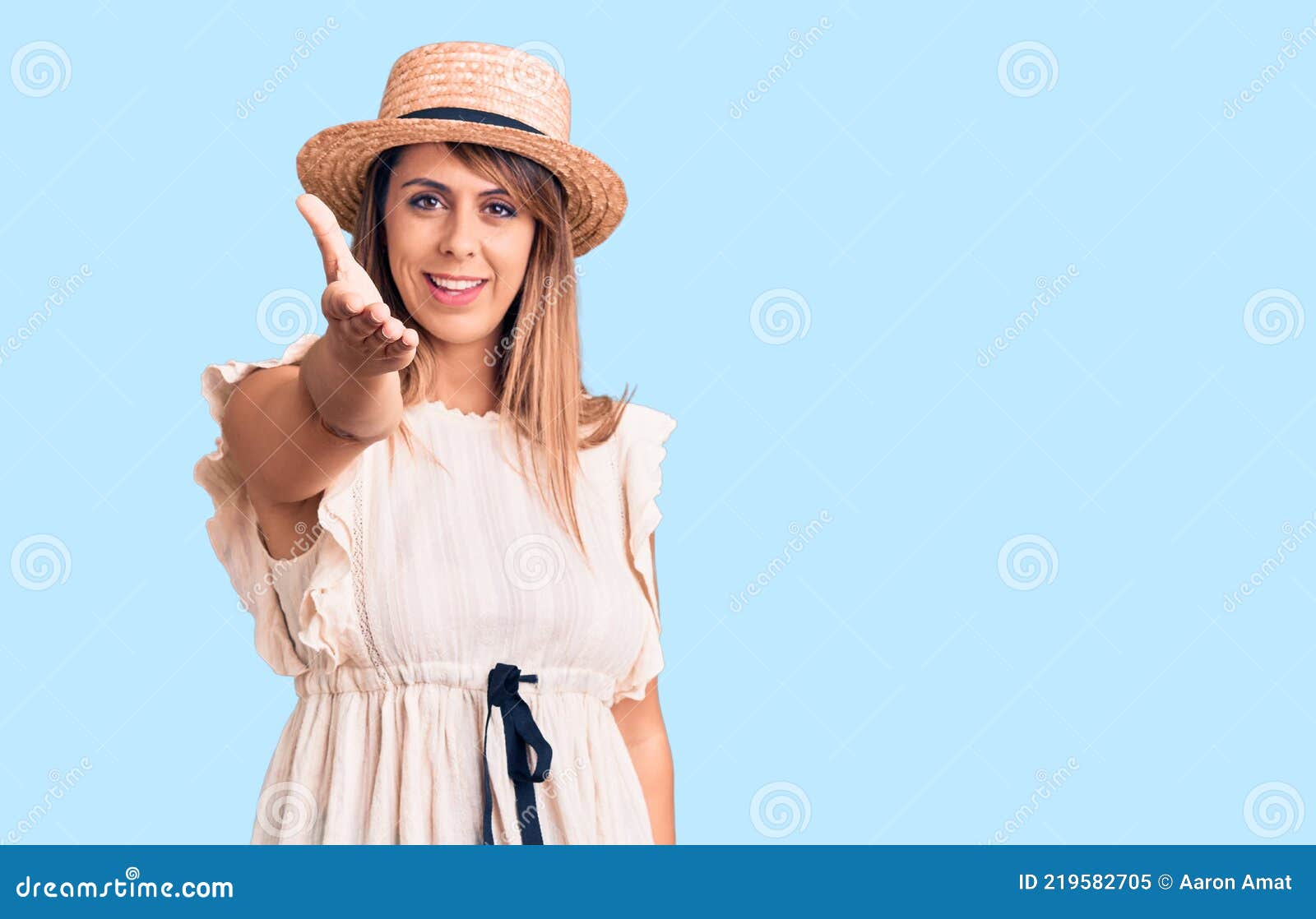 young beautiful woman wearing summer hat and t-shirt smiling friendly offering handshake as greeting and welcoming
