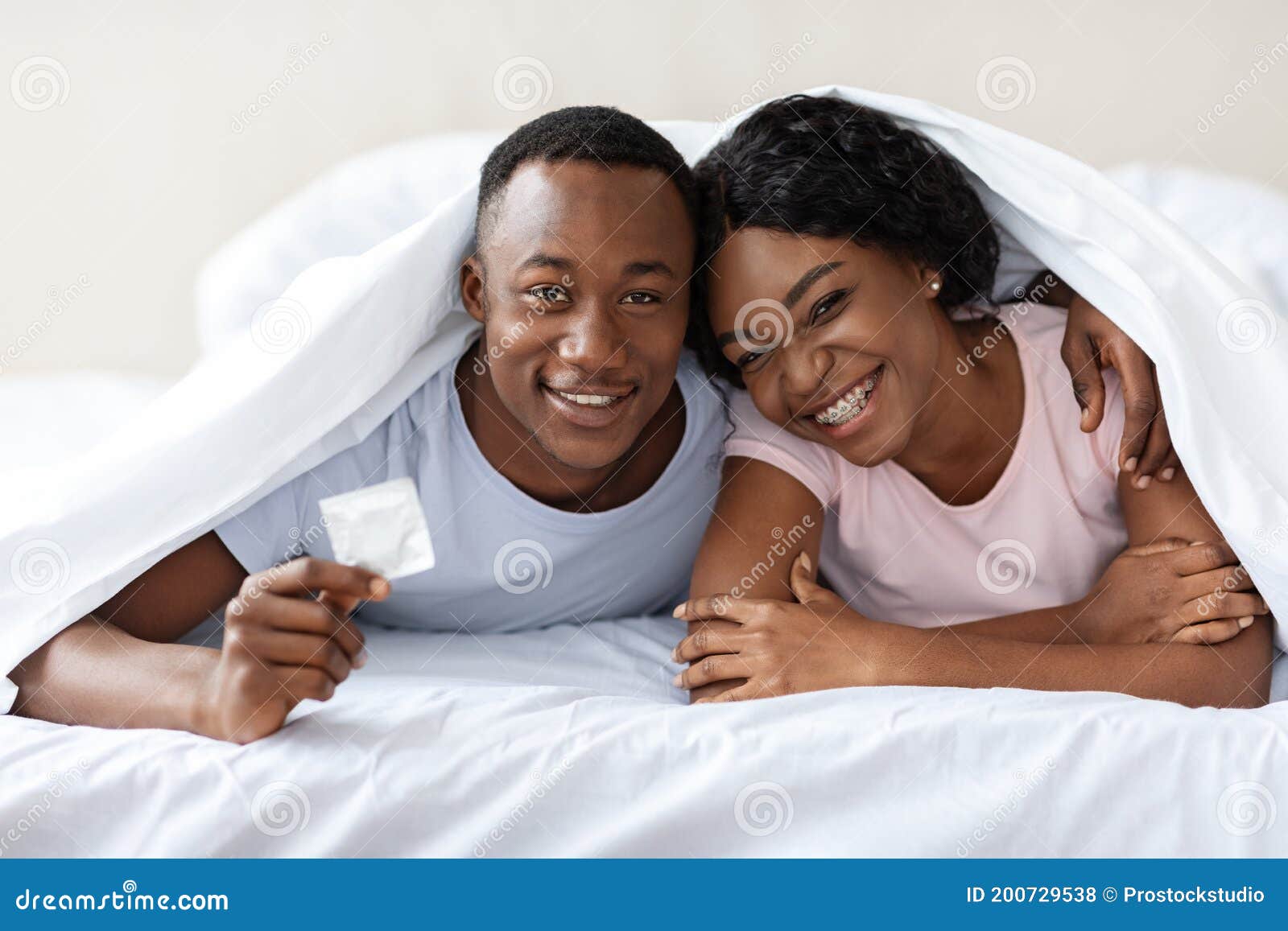 Young Black Couple Smiling and Holding Condom, Bedroom Interior Stock Photo 