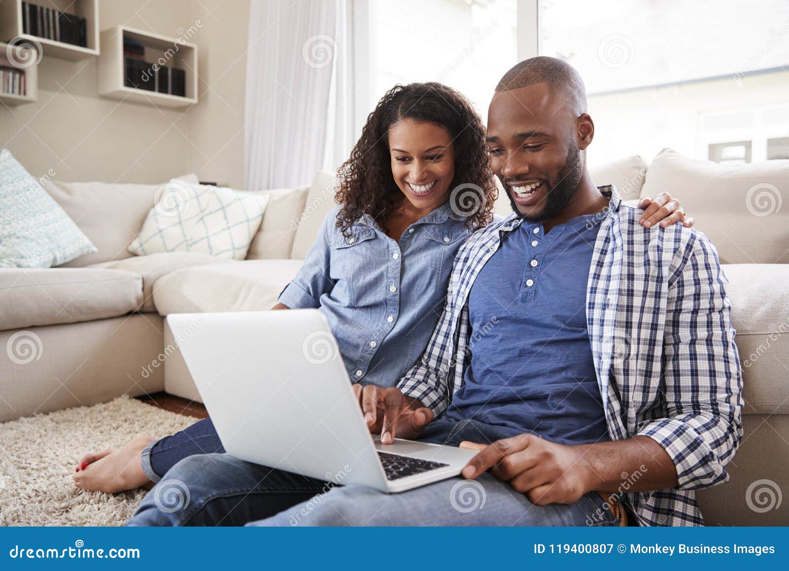 young black couple using laptop sitting on the floor at home