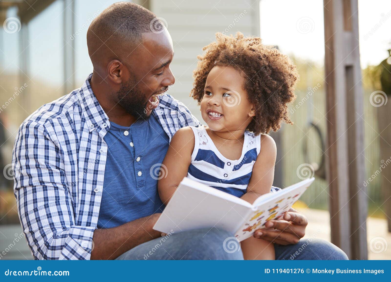 young black father and daughter reading book outside