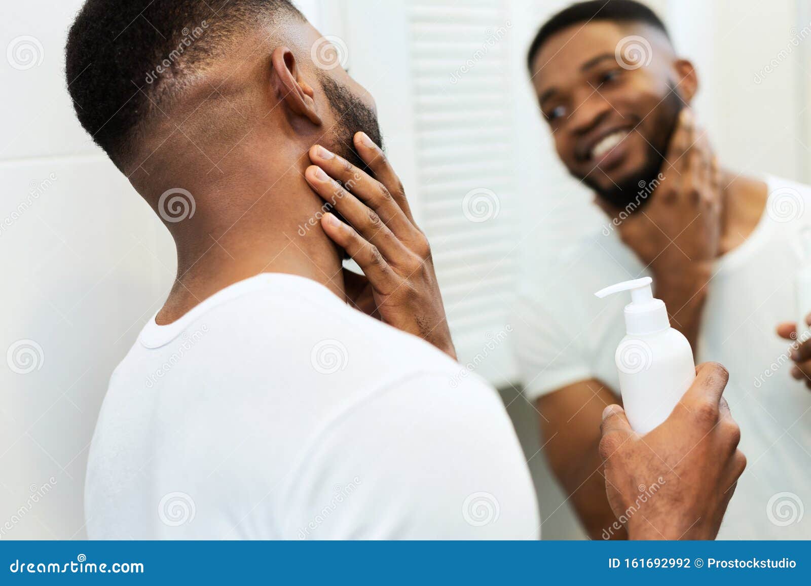 young black man applying moisturizer on beard in bathroom