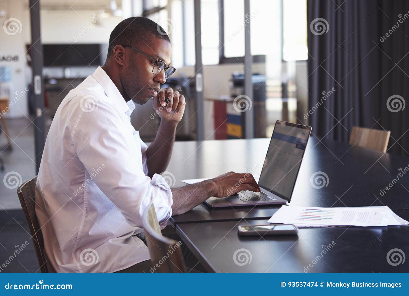 young black man in wearing glasses using laptop in office