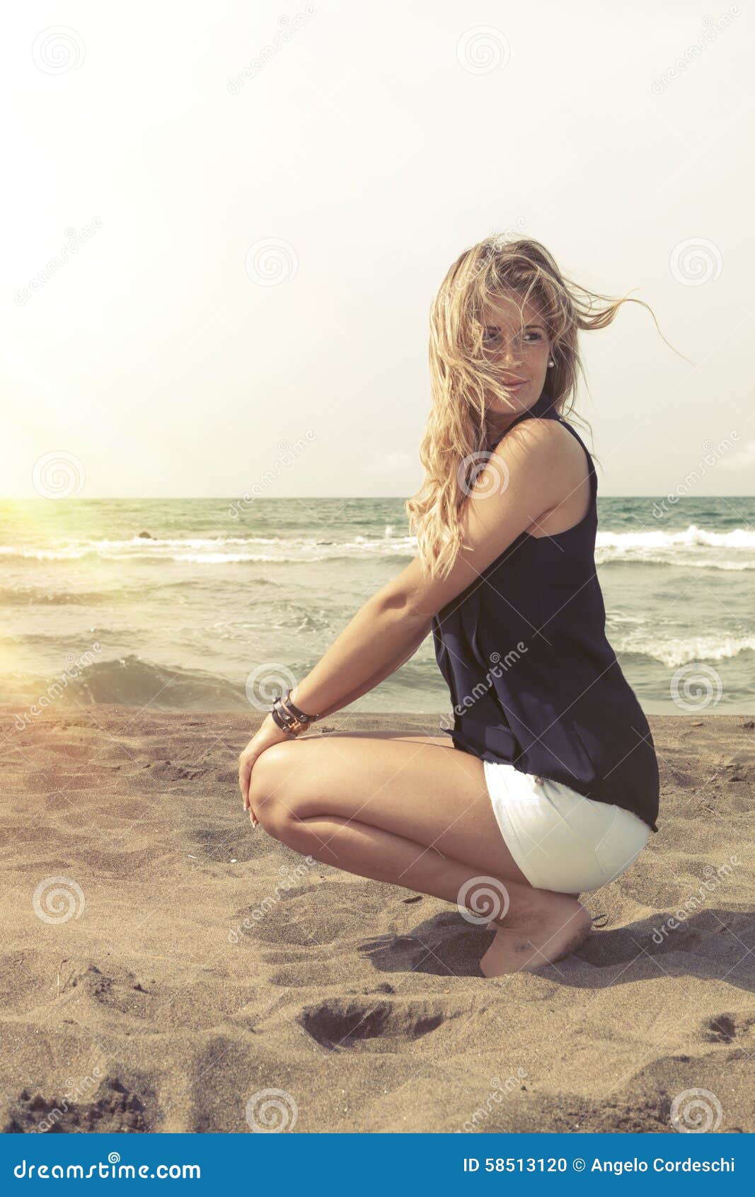 Young Blonde Hair Girl Relaxing On The Beach Sand. Wind In 