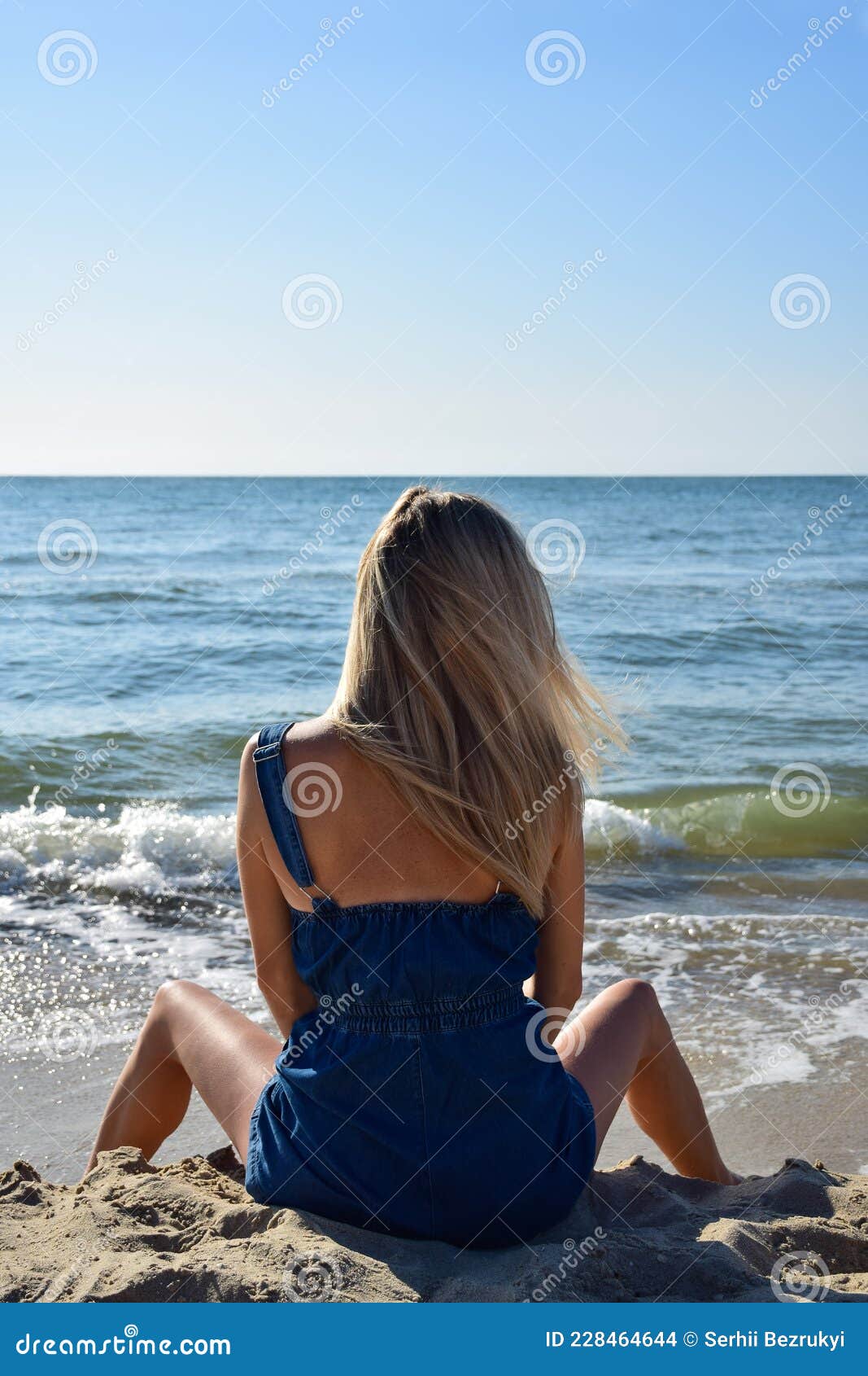 A Young Blonde Girl Sits in the Morning on the Beach with Her Legs ...