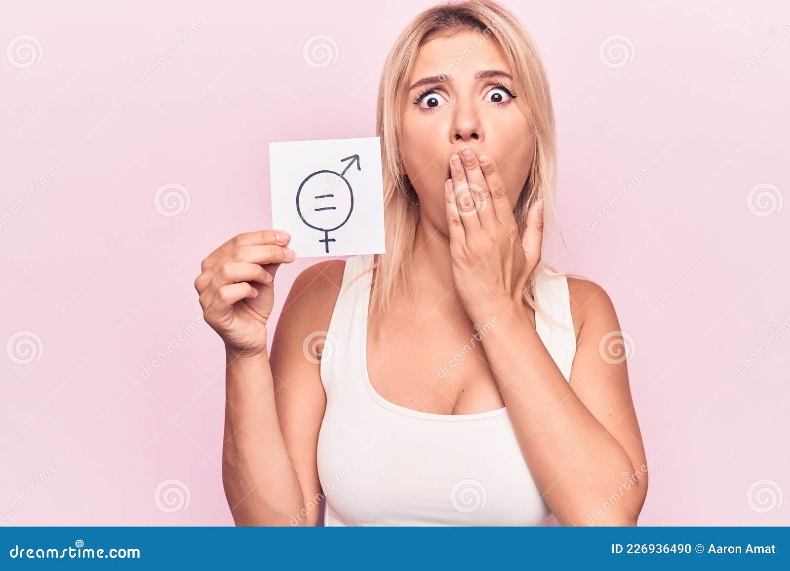 Young Blonde Woman Asking for Sex Discrimination Holding Paper with Gender Equality Message Covering Mouth with Hand, Shocked and Stock Photo image image