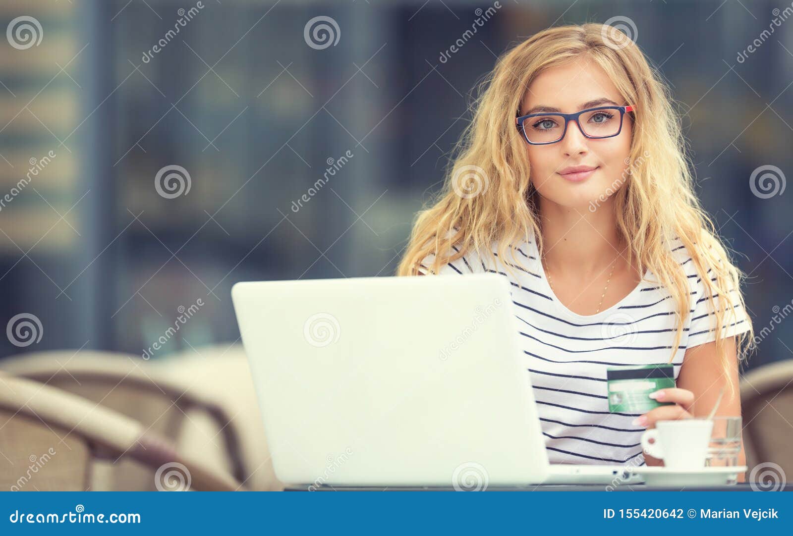 young blonde woman holding credit card and using laptop computeron the terrace of the caf
