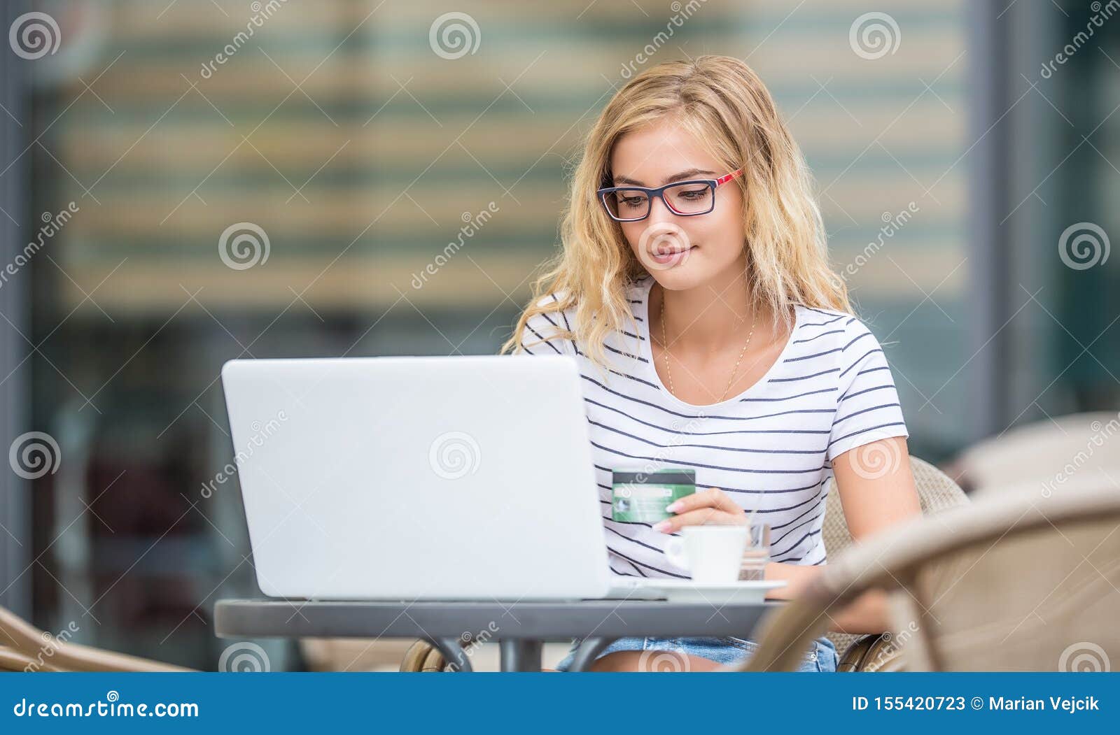 young blonde woman holding credit card and using laptop computeron the terrace of the caf