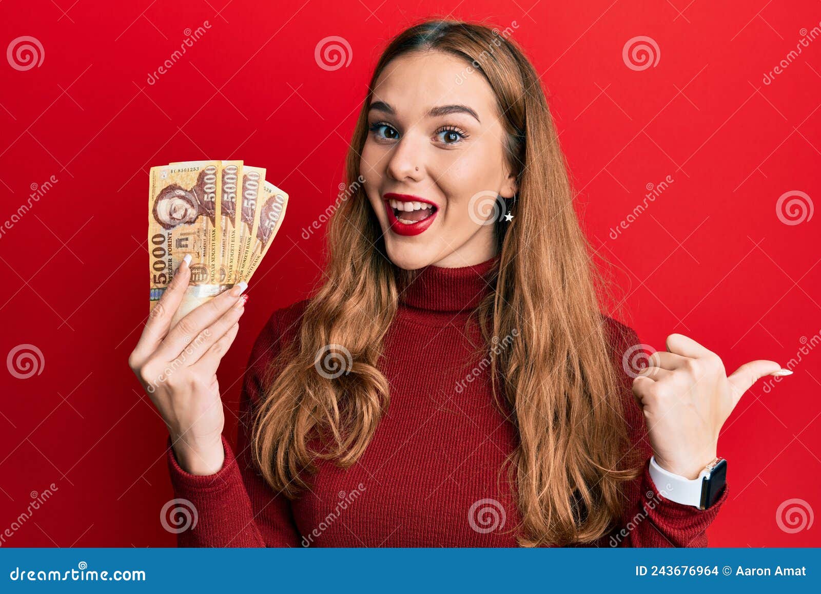 Young Blonde Woman Holding 5000 Hungarian Forint Banknotes Pointing Thumb Up To The Side Smiling