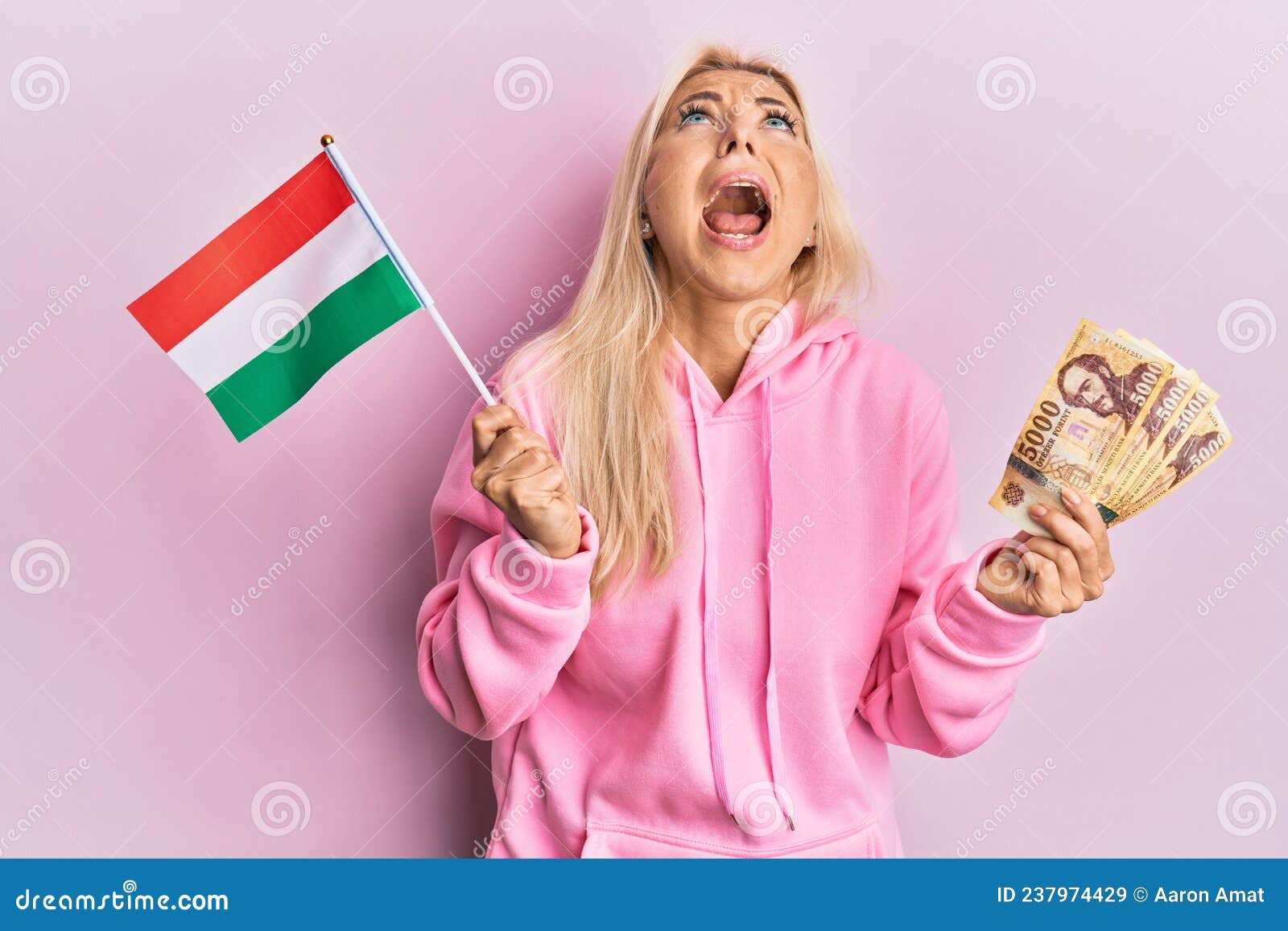 Young Blonde Woman Holding Hungary Flag And Forint Banknotes Angry And Mad Screaming Frustrated