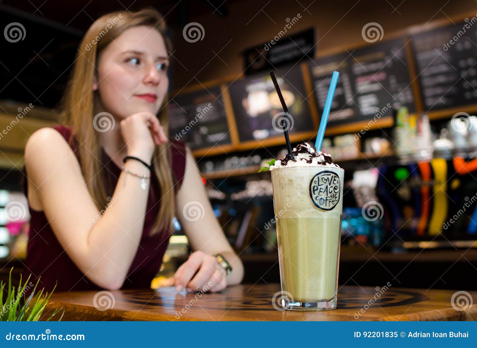 young blonde woman in local cafe at wooden table drink frappe wi