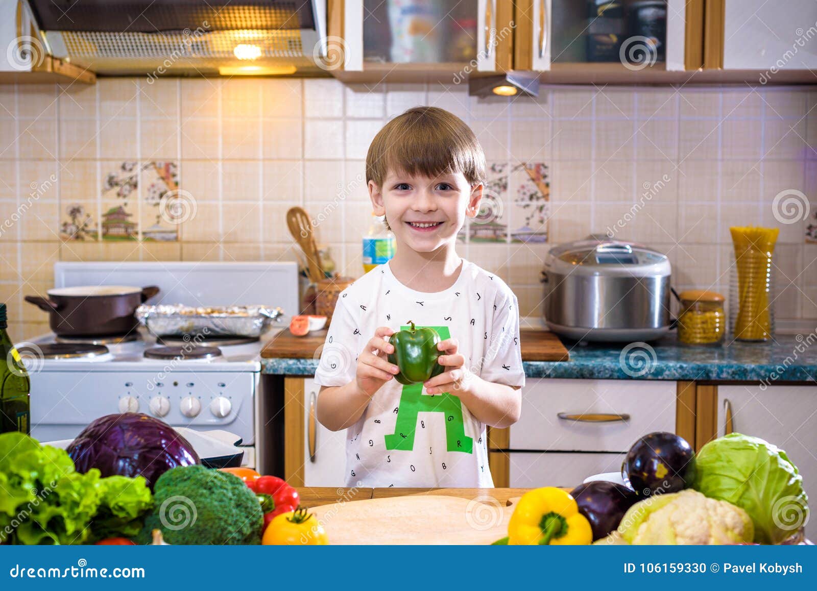 The Young Boy in Cooking Standing in the Kitchen Near Table with Stock