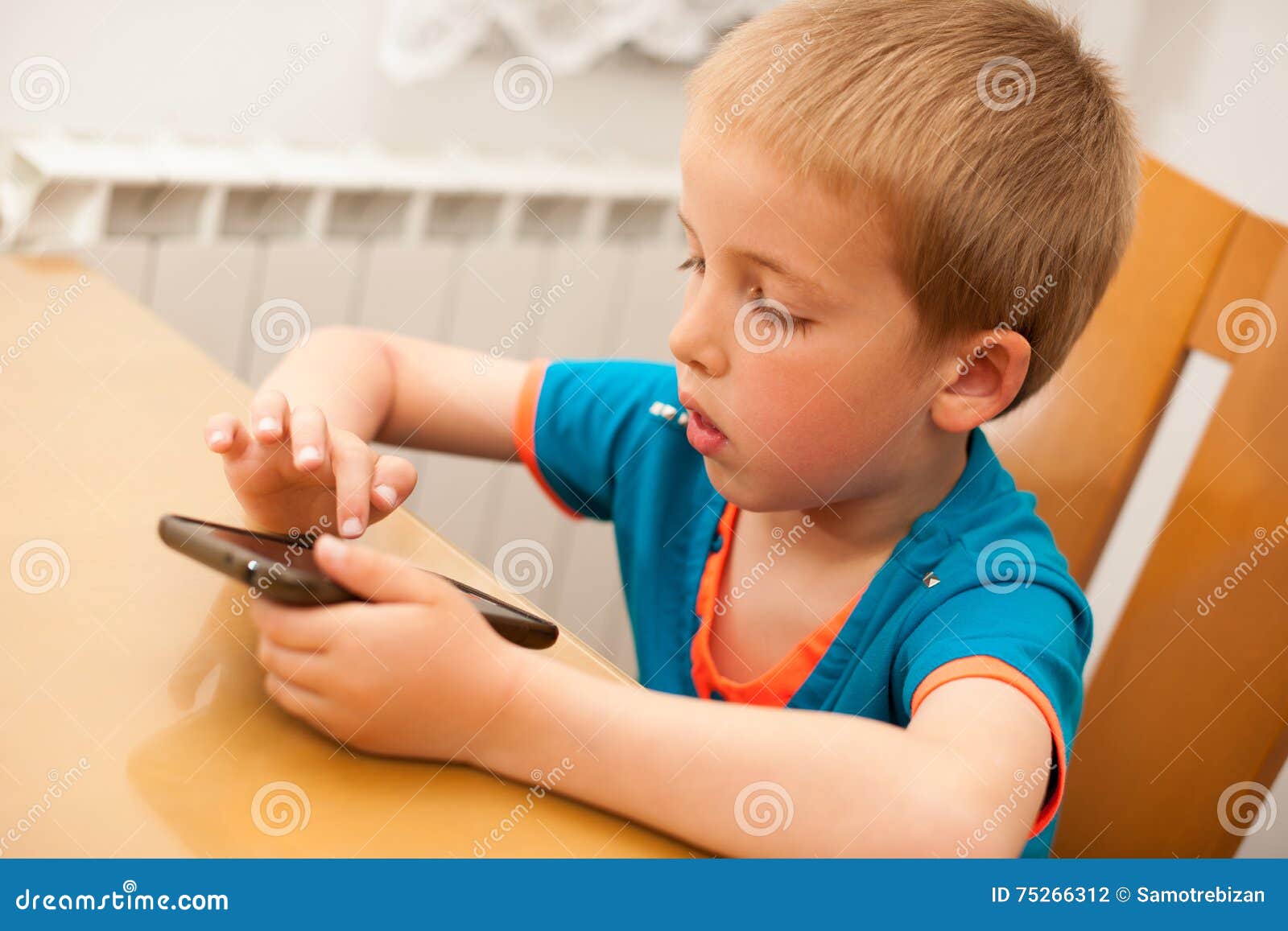 Young Boy Plays with a Smart Phone at Kitchen Table Stock Photo Image