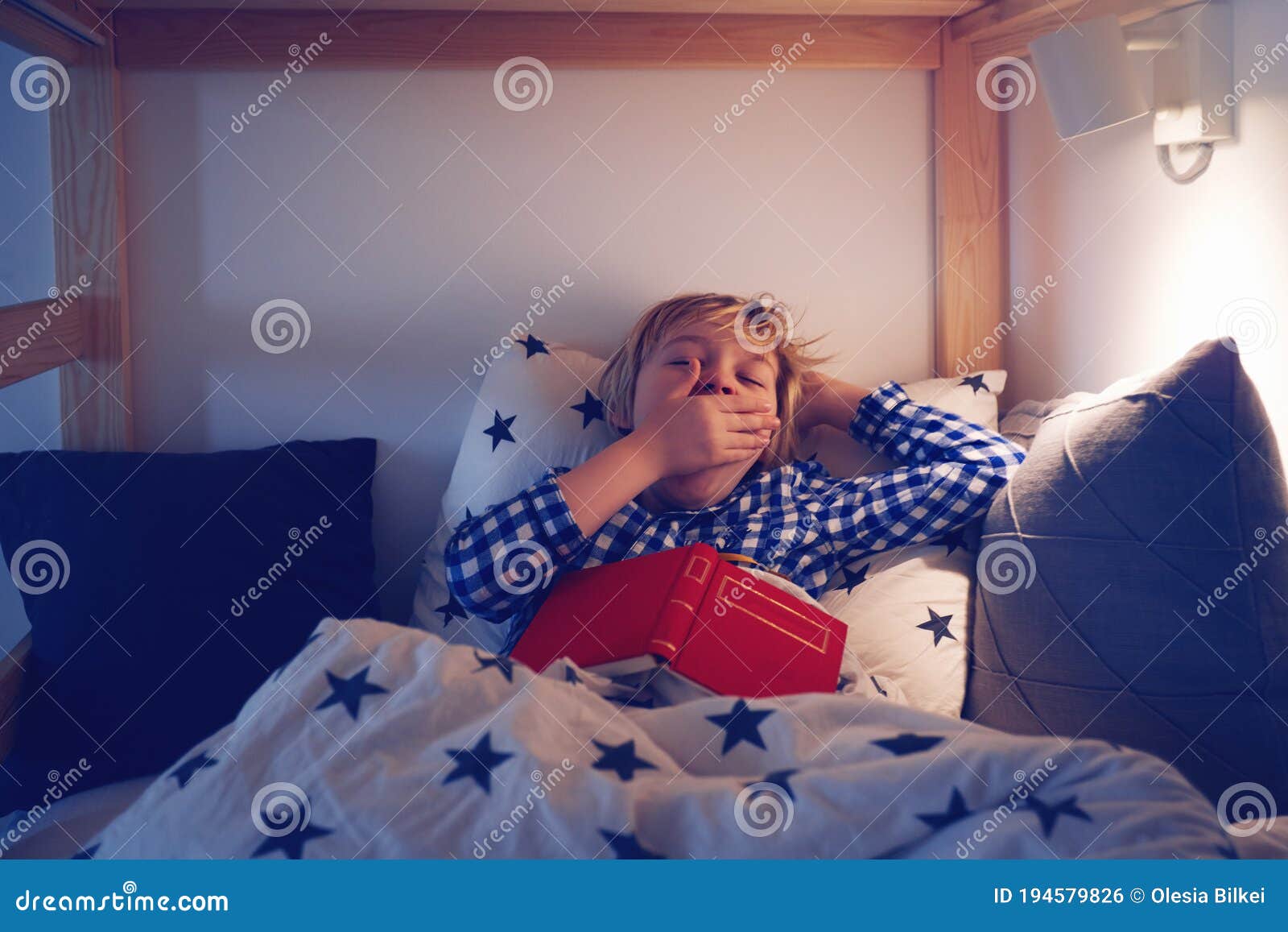 Young Boy Yawning While Laying In The Bed And Reading A Book Before