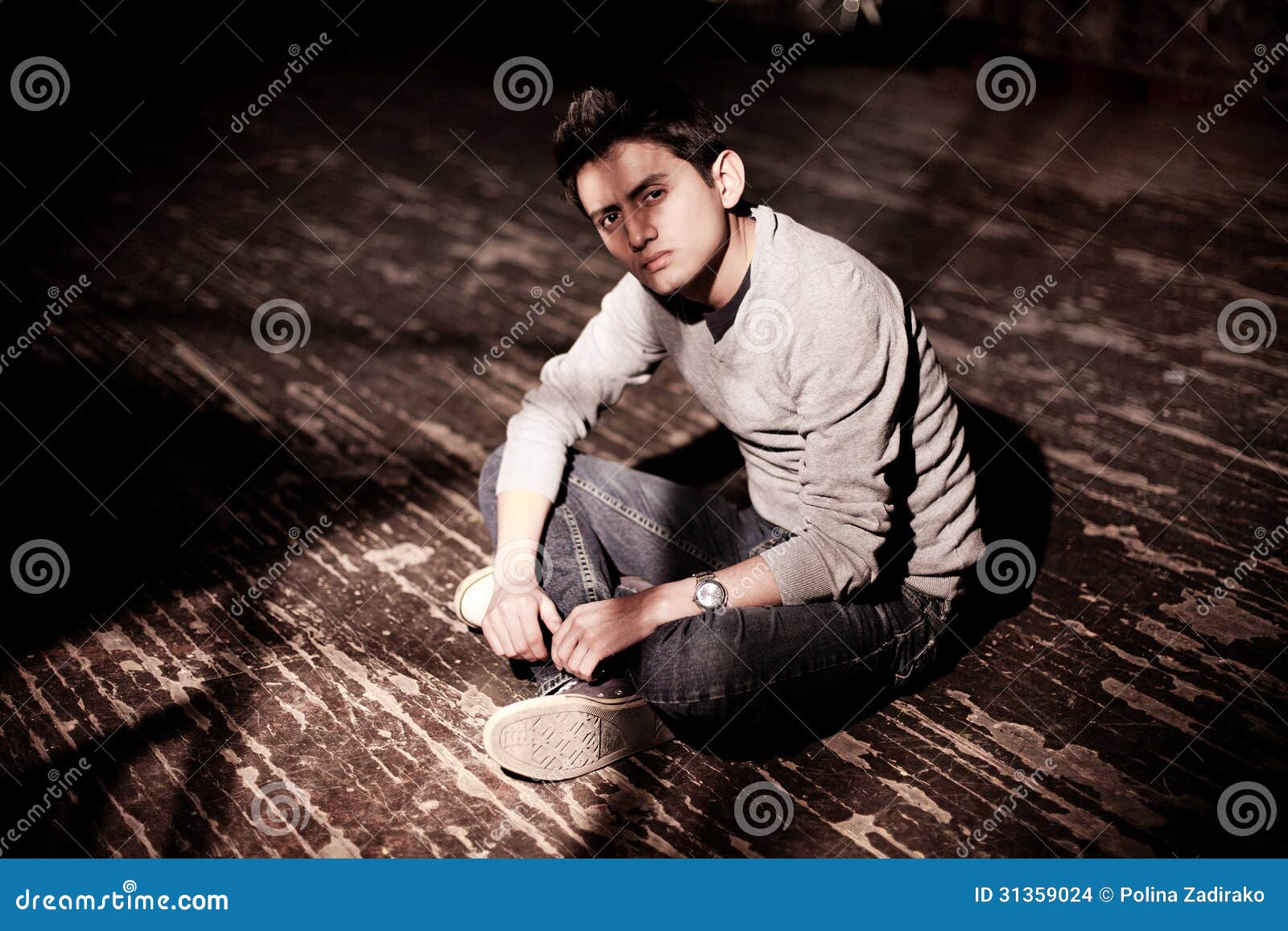 a young brunet man sitting on a wooden floor