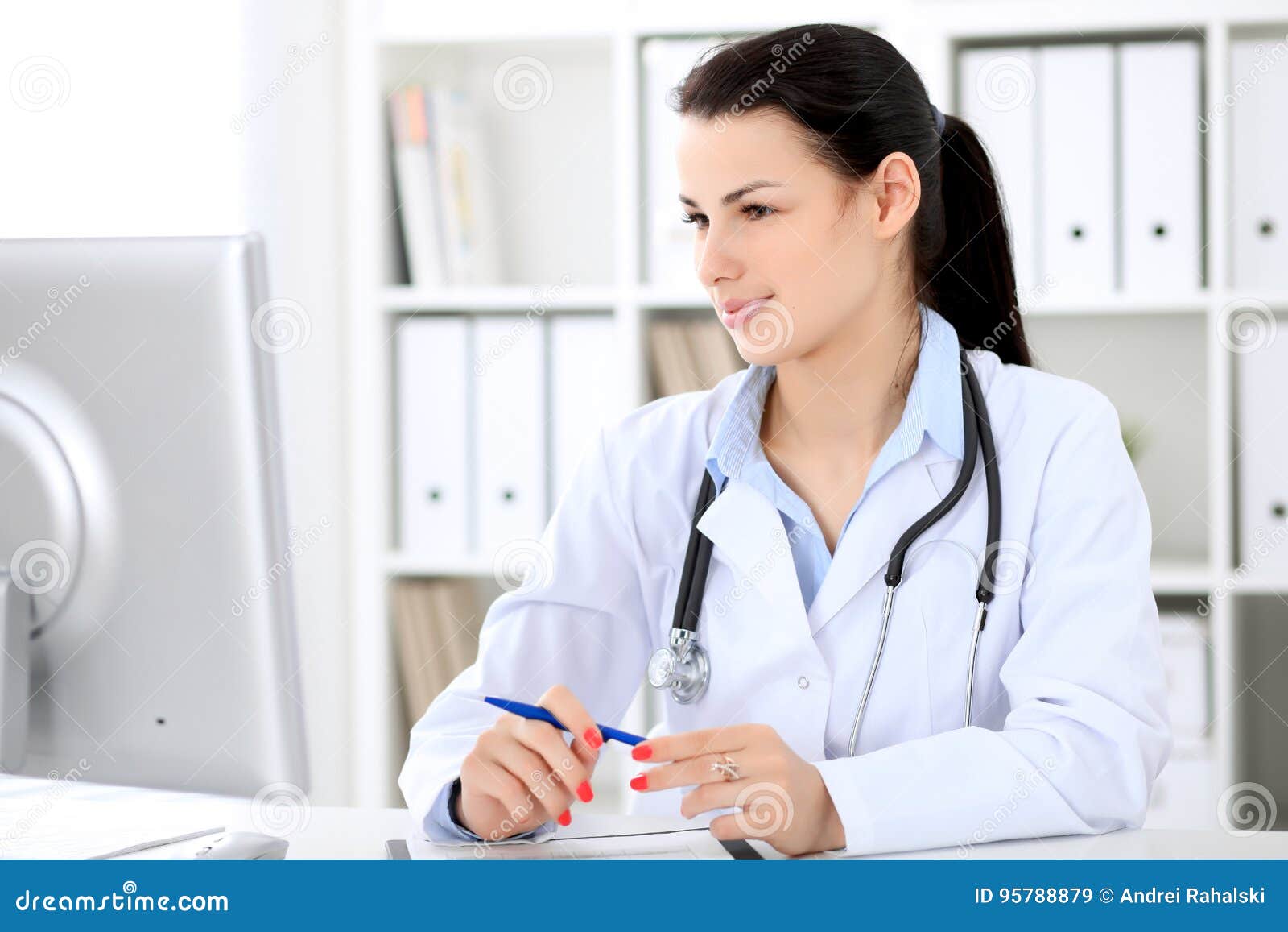 Young Brunette Female Doctor Sitting At The Table And Working By